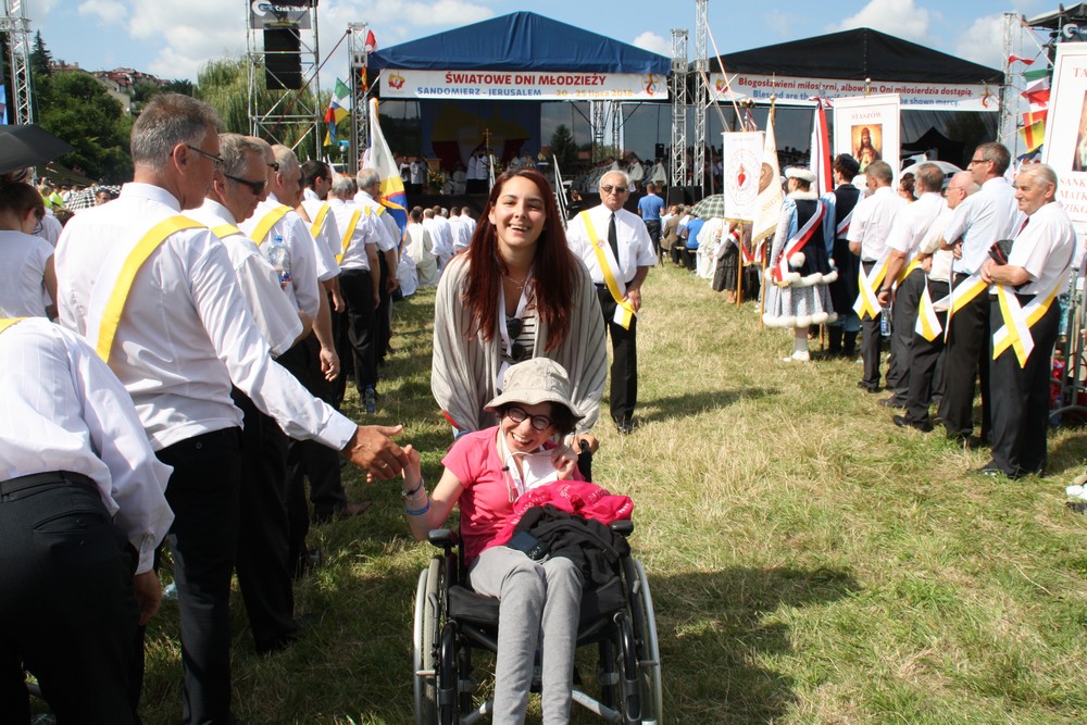 une personne handicapée entre 2 rangées de prêtres