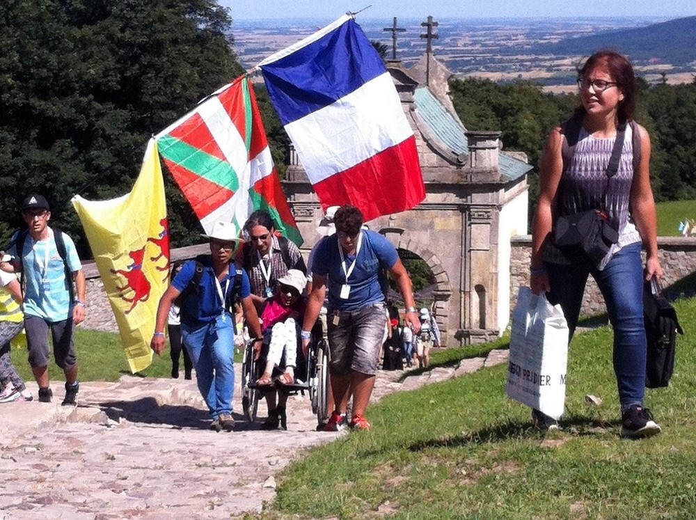 des personnes portent à bout de bras un fauteuil avec une personne handicapée