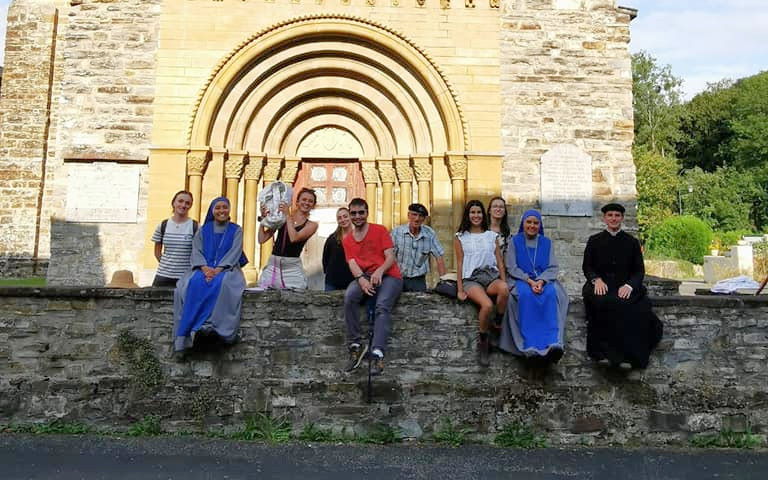 des jeunes et des religieux assis sur un mur, devant une église