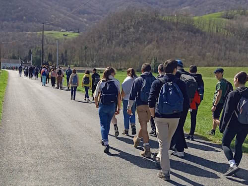 jeunes, vus de dos, marchant devant eux, sur une route, en arrière plan les montagnes